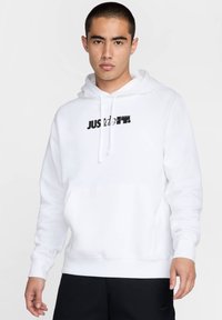 Sudadera blanca con bolsillo canguro, que presenta un logo negro impreso "JUST DO IT". Fabricada con una mezcla de algodón, cuenta con una capucha ajustable con cordón.