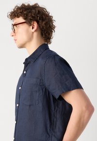 Marineblauwe linnen overhemd met korte mouwen en een borstzakje, met een button-down kraag en een gladde textuur.