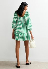Robe à rayures vertes et blanches avec des manches bouffantes, un ourlet volé, et un dos nu. Associée à un petit sac à main tressé blanc et des sandales noires.