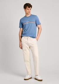 Blå bomull t-skjorte med en horisontal stripete design, kombinert med kremfargede cargo-bukser med lommer og hvite sneakers med brune detaljer.
