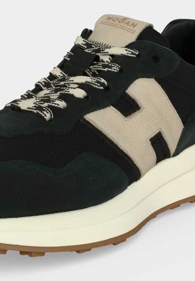 Κοντινό πλάνο σε μαύρο και μπεζ sneaker Hogan με κορδόνια με σχέδια, μεγάλο μπεζ λογότυπο "H" και λευκή σόλα με καφέ πέλμα.