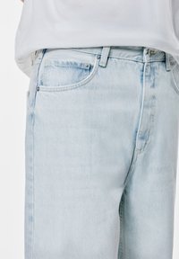 Jeans din denim albastru deschis cu o croială dreaptă, având un design cu cinci buzunare, nasture metalic și o ușoară decolorare în zona coapselor.
