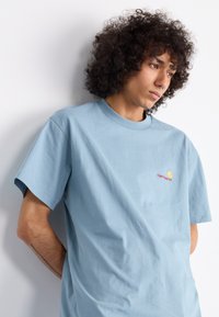 Blue cotton t-shirt with a round neckline, short sleeves, and a small Carhartt logo in red and yellow on the left chest.