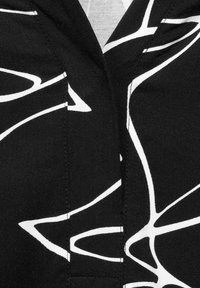 Svart tyg med ett djärvt, abstrakt mönster av vita linjer i varierande tjocklek. Slät textur med rena sömmar och stygn detaljer.