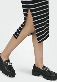 Mocasines negros gruesos con un acento de cadena plateada. Los zapatos tienen un acabado de cuero suave y una suela gruesa y texturizada.