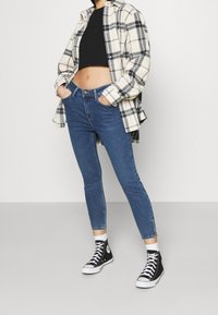 Blå skinny jeans i denim med hög midja, kombinerade med en svart croptop och en krämfärgad rutiga skjorta, kompletterad med svarta högsneakers.