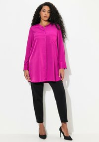 Fuchsienfarbene Langarm-Tunika mit Knopfdetail und einer Brusttasche, kombiniert mit schwarzen Slim-Fit-Hosen und schwarzen High Heels.