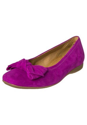 Fioletowe zamszowe płaskie buty z kokardką na czubku i jasnobrązową podeszwą, ukazujące wewnętrzną wyściełaną wkładkę.