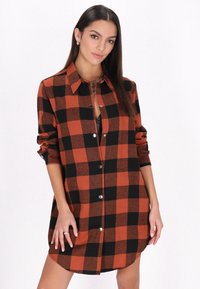 Abito camicia a scacchi rosso e nero in flanella, con chiusura a bottoni sul davanti, maniche arrotolate e orlo curvo.