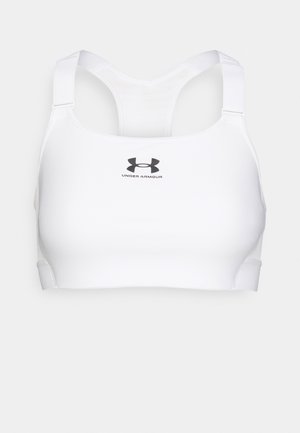 Biała sportowa biustonosz wykonana z gładkiego materiału, z regulowanymi ramiączkami i jednolitą szeroką gummą. Z przodu widoczny czarny logo "Under Armour".