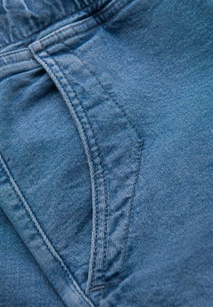 Sininen farkkukangas, jossa on hieman karhea pinta, esittelee taskusauman ja kontrastiväriset ompeluyksityiskohdat. Kankaan näyttää olevan kestävä ja joustava.