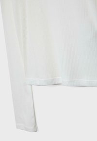 Ourlet et bords des manches d'un t-shirt blanc à manches longues côtelé avec des coutures visibles sur un fond uni.