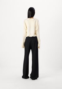 Krémová hedvábná blůza s dlouhými rukávy a rozparkem na manžetách, spárovaná s černými širokými kalhotami s dvěma zadními kapsami a hladkou texturou.