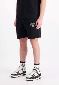 Zwarte katoenen shorts met witte "BLCKBNNS" logo, gecombineerd met zwart-witte sneakers met een patroon en crew sokken. Eenvoudig, relaxte pasvorm.