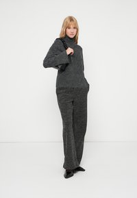 Suéter de lã cinza com gola alta e um corte solto, combinado com calças cinzas largas. Os acessórios incluem uma bolsa estruturada preta.