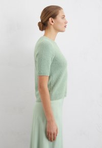Maglione corto verde chiaro, con trama e maniche corte, con scollatura rotonda, abbinato a una gonna liscia verde menta, esposto su uno sfondo neutro.