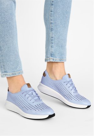 Baskets bleu clair avec un design perforé, forme arrondie, matériau supérieur doux, semelle blanche et accent marron sur le talon.