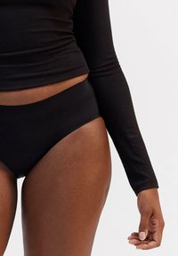 Top a maniche lunghe nero a coste con silhouette aderente, abbinato a slip neri a vita alta. Texture liscia e design minimalista.