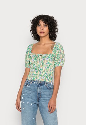 Top crop floral com decote quadrado, mangas curtas e bufantes, e um padrão em verde, azul e amarelo. Combinado com jeans azuis desfiados.