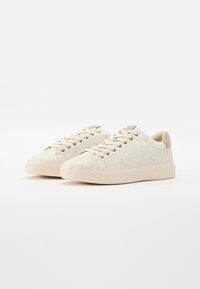 Paire de baskets basses beiges avec une texture à motif serpent, fermeture à lacets à l'avant et semelles beige clair sur fond blanc uni.