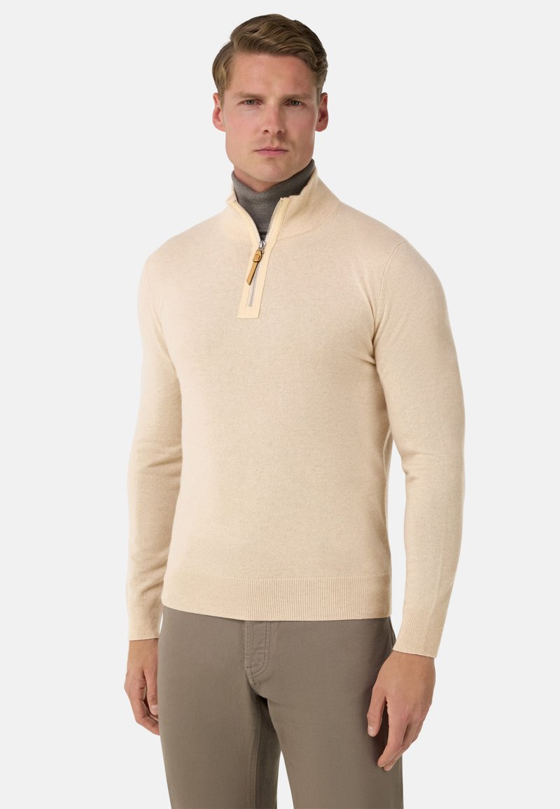 Pull-over zippé beige avec col montant, fabriqué en matériau doux. Présente une fermeture éclair contrastante ainsi que des poignets et un ourlet côtelés.