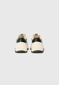Rear view of athletic shoes featuring a cream midsole, black heel, green and tan accents, and textured detailing on upper panel.