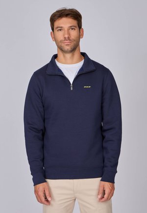 Sweatshirt zippé bleu marine en tissu doux, avec col montant et poignets côtelés, arborant un petit logo jaune sur la poitrine.