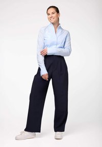 Camicia azzurra chiara con colletto e maniche lunghe abbinata a pantaloni blu scuro a vita alta e sneakers bianche; tessuto morbido e vestibilità sartoriale.