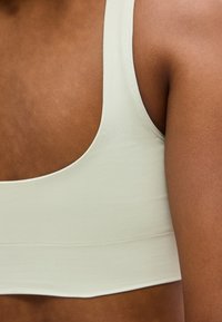 Gros plan sur une personne à la peau foncée portant un débardeur beige clair, montrant l'épaule, le haut du dos et la zone du bras.