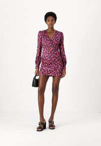 Rochie scurtă, ajustată geometric, cu mâneci lungi, într-un model abstract vibrant de roz și mov. Asortată cu sandale negre cu toc și o geantă mică.