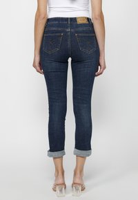 Jeans skinny azul oscuro con puños enrollados, que cuentan con bolsillos traseros con costuras decorativas y una etiqueta de marca en la cintura.