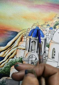 Aquarel kunstwerk met witte gebouwen met blauwe koepels, een kustlijn en een achtergrond van een zonsondergang; een penseel vastgehouden in een hand.