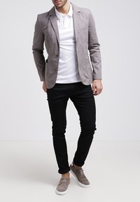 Jasnoszary blezer z dwoma guzikami, noszony na białej koszulce polo. Czarnie dopasowane spodnie i szare buty wsuwane dopełniają strój.