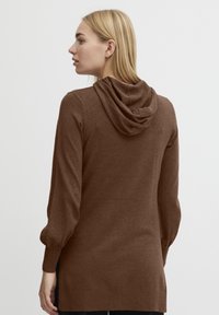 Hoodie marron en matériau doux, avec une coupe décontractée, des manches longues avec poignets, et une grande capuche drapée à l'arrière.