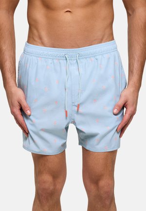 Pantalones cortos de baño azul claro con estampado pequeño de flamencos rosas, cintura elástica y cordón, usados por un hombre de pie con las manos a los lados.