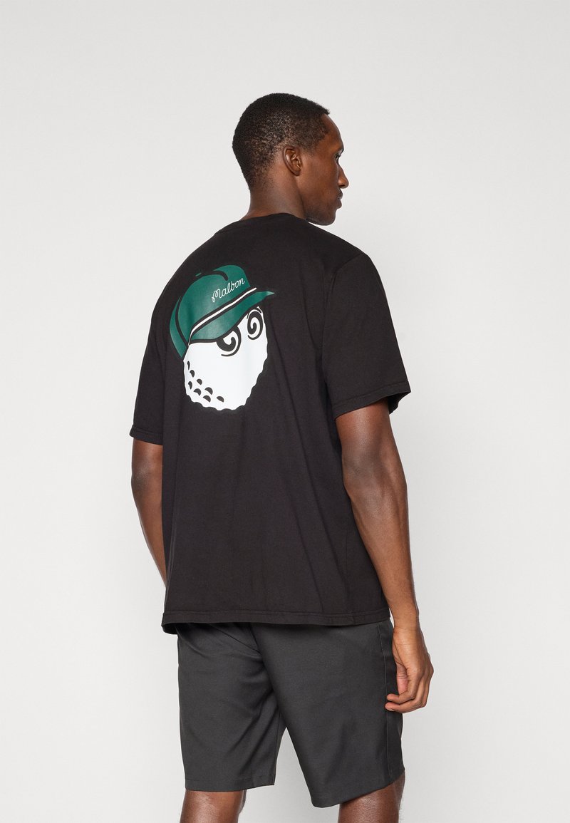 Sort bomulds t-shirt med korte ærmer, prydet med en hvid grafik af et ansigt med en grøn kasket på ryggen. Blød tekstur og afslappet pasform.