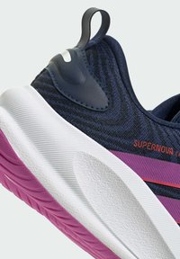 Ciemnoniebieski but sportowy z teksturowaną cholewką, białą podeszwą środkową i różową podeszwą zewnętrzną. Posiada pętelkę na pięcie oraz czerwone logo "SUPERNOVA".