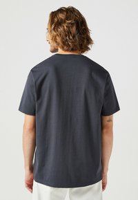 Mörkgrå, kortärmad t-shirt med rund halsringning, tillverkad av bomull, med en slät yta och en avslappnad passform, som visar upp en enkel, ren design.