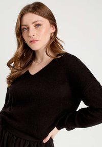 Black knit sweater with a v-neck design, featuring long sleeves and a soft texture, worn with a black skirt. Minimalist style.