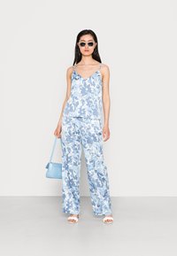 Conjunto de duas peças com padrão floral azul claro, apresentando uma blusa sem mangas com alças finas e calças de perna larga. Acompanhado de uma bolsa azul clara.