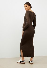 Ribbed braunes langärmliges Kleid mit seitlichen Schlitz, figurbetontem Design und tiefem Rückenausschnitt, kombiniert mit weißen Sneakern mit Marineblau-Akzenten.