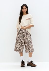 Tricou oversized bej cu pantaloni scurți leopard. Tenisi maro asortați cu șosete albe. Material moale, croi relaxat și detalii îndrăznețe în model.