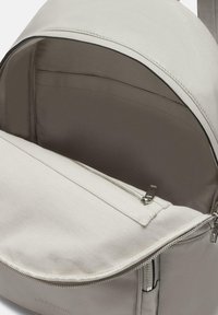 Hellgrauer Leder-Rucksack mit einem runden Reißverschluss. Das Innere ist mit einem Stofffutter ausgestattet und verfügt über eine Reißverschlusstasche für sicheren Stauraum.