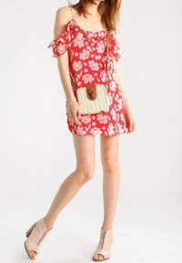 Vestido floral rojo con mangas acampanadas, de largo por encima de la rodilla. Combinado con un bolso cruzado de mimbre y botas de tacón con cremallera en el tobillo de color beige.