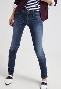 Smala jeans i mörkblå denim. Har en mjuk yta med subtil blekning, fem fickor och knappknäppning i metall. Kombineras med tvåtonade skor.