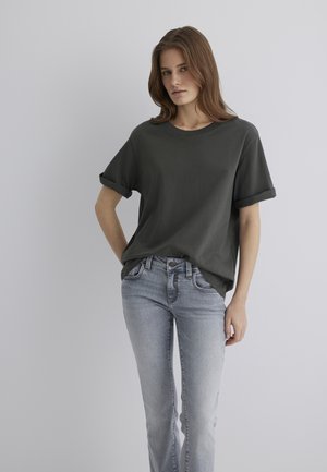 Dunkelgrünes Baumwoll-T-Shirt mit umgeschlagenen kurzen Ärmeln, kombiniert mit hellblauen Jeans aus Denim mit eng anliegendem Schnitt und Standardtaschen.