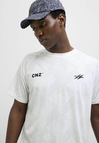 Hvid trænings t-shirt med geometrisk mønster, korte ærmer og sorte logoer "CNZ" samt en lyn. Struktureret stof.