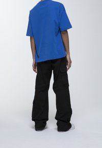 Modré bavlněné tričko s krátkým rukávem, kombinované s černými cargo kalhotami s kapsami. Šedé tenisky doplňují celý outfit.