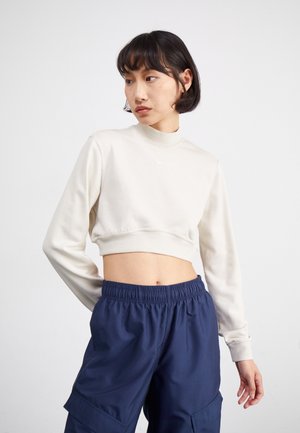 Light beige cropped sweatshirt with a high neckline and long sleeves. Paired with navy blue, loose-fitting cargo pants featuring side pockets.