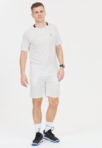 Vaaleanharmaa urheiluasu, jossa on lyhythihainen paita ja shortsit, joissa on pieni kultainen logo. Mustat yksityiskohdat kauluksessa; yhdistetty mustiin kenkiin.